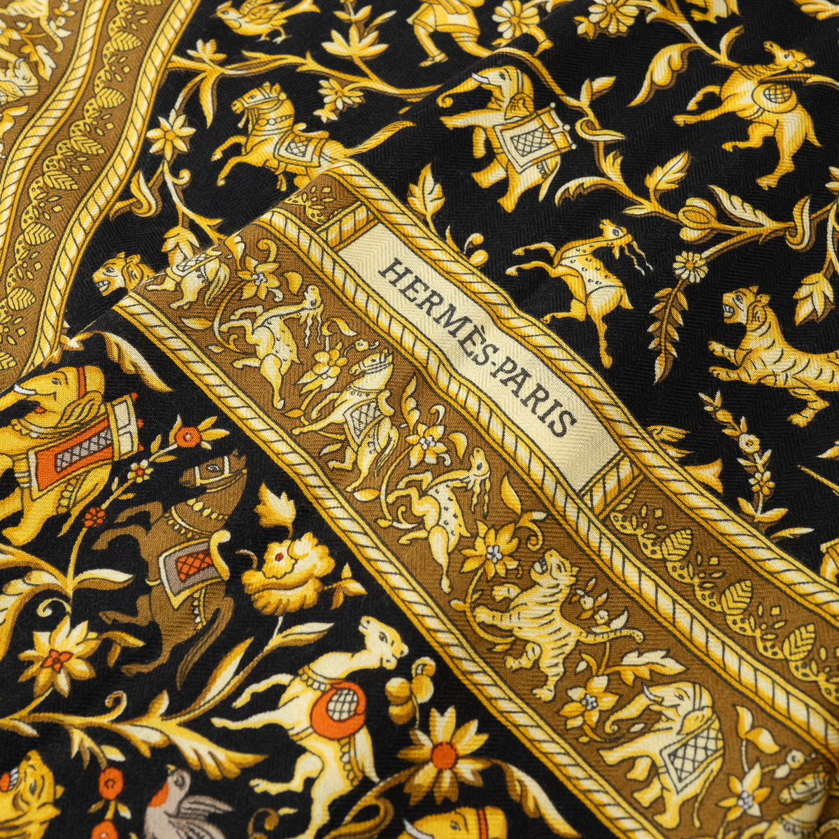 Close up of Hermes Black and Gold Silk Chasse En Inde Scarf with motifs of Hunters, Birds, Lions, Tigers, Elephants, Gazelles, Horses, and Flowers 