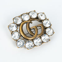 Gucci aged gold brooch with 'GG' logo and crystal stones on a white background