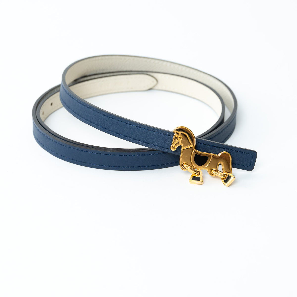 Hermes Blue leather belt with a gold horse charm on a white background