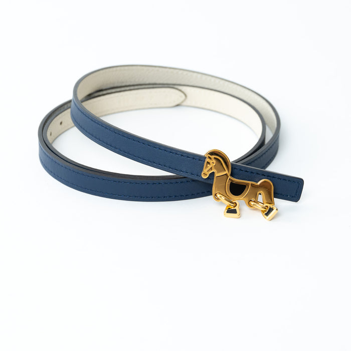 Hermes Blue leather belt with a gold horse charm on a white background