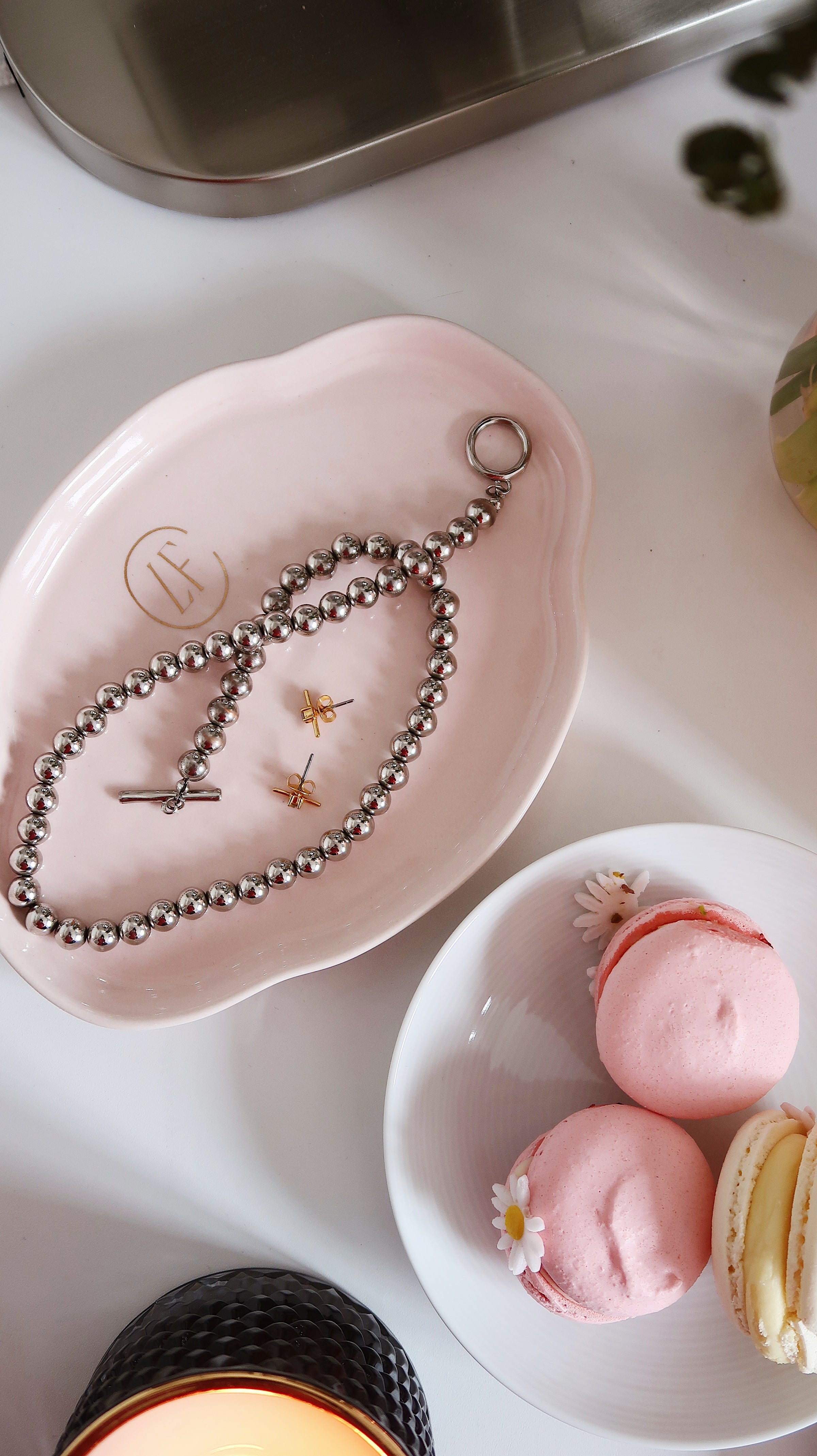 An  image displaying a pink luxury finds consignment jewellery tray with earrings and a necklace,  and a small dish with three macaroons