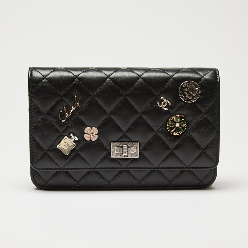 Black quilted Chanel wallet on chain with various Chanel logos and charms